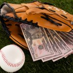 dollar banknotes in baseball glove near ball on green grass, sports betting concept